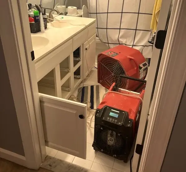 Air mover and dehumidifier drying a bathroom vanity after an overflow