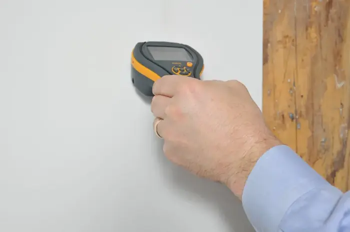 Hand holding a pinless moisture meter against a wall