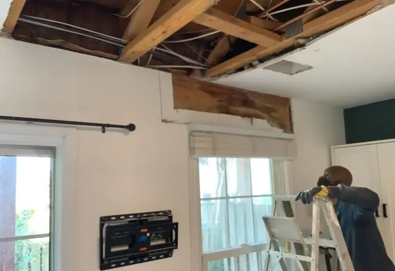 Ceiling opened to the rafters after a roof leak, with a worker on a ladder