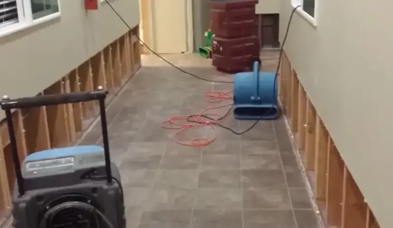 Dehumidifier and air mover drying a hallway after the lower drywall was cut out