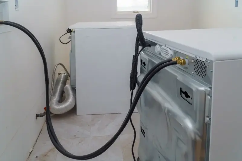 Washer pulled out from the wall with its supply and drain hoses exposed