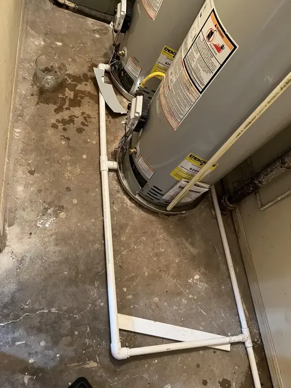 Water pooled on the floor around a leaking water heater in a utility closet
